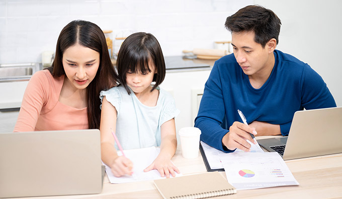 Asian American mother and father helping their young female child with remote learning