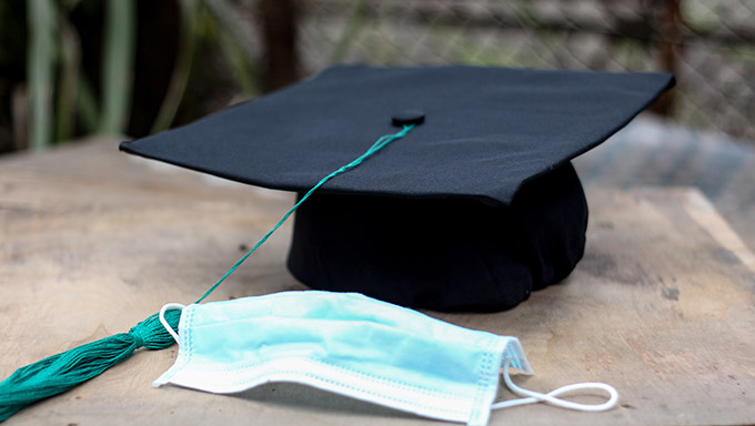 Black graduation cap with blue tassel standing on a background with medical mask. Horizontal image