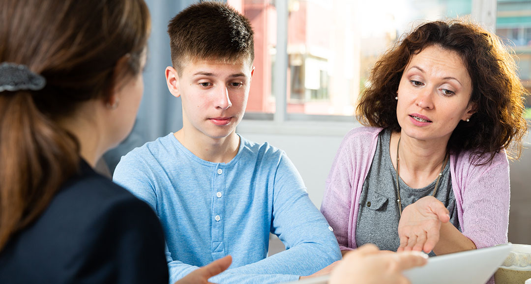 Focused teenage boy and his mother sitting at home table, participating in person centered planning for adult life as part of the students transition plan.
