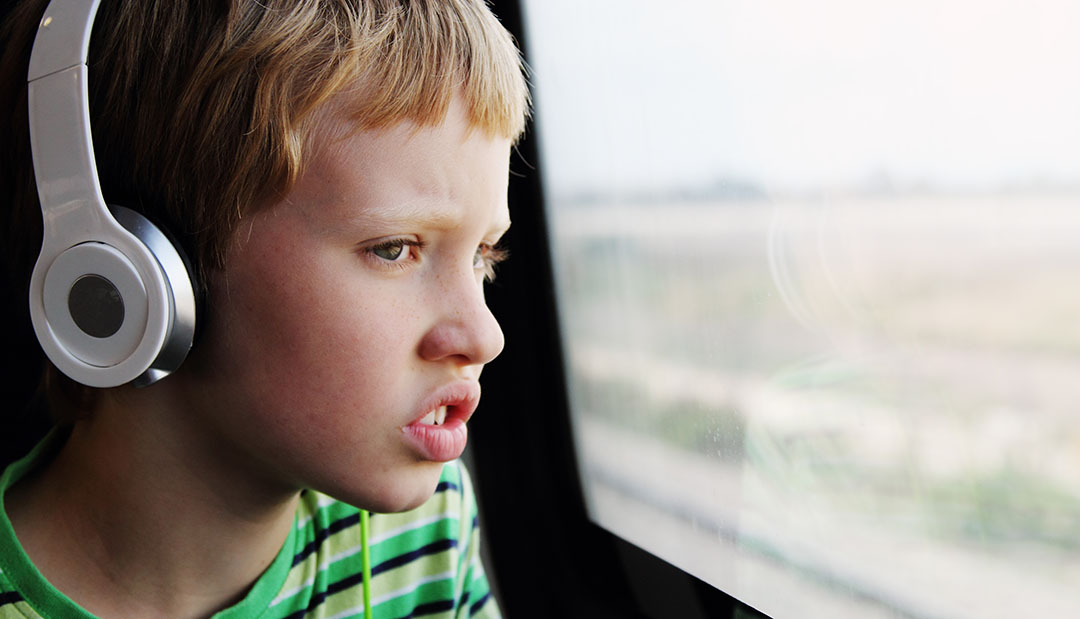 Young male student with disability on school bus wearing headphones looking worried