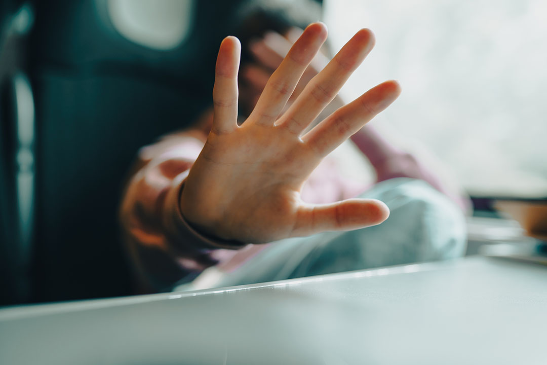 Student holding out his palm-forward hand defensively and hiding his face with the other hand.