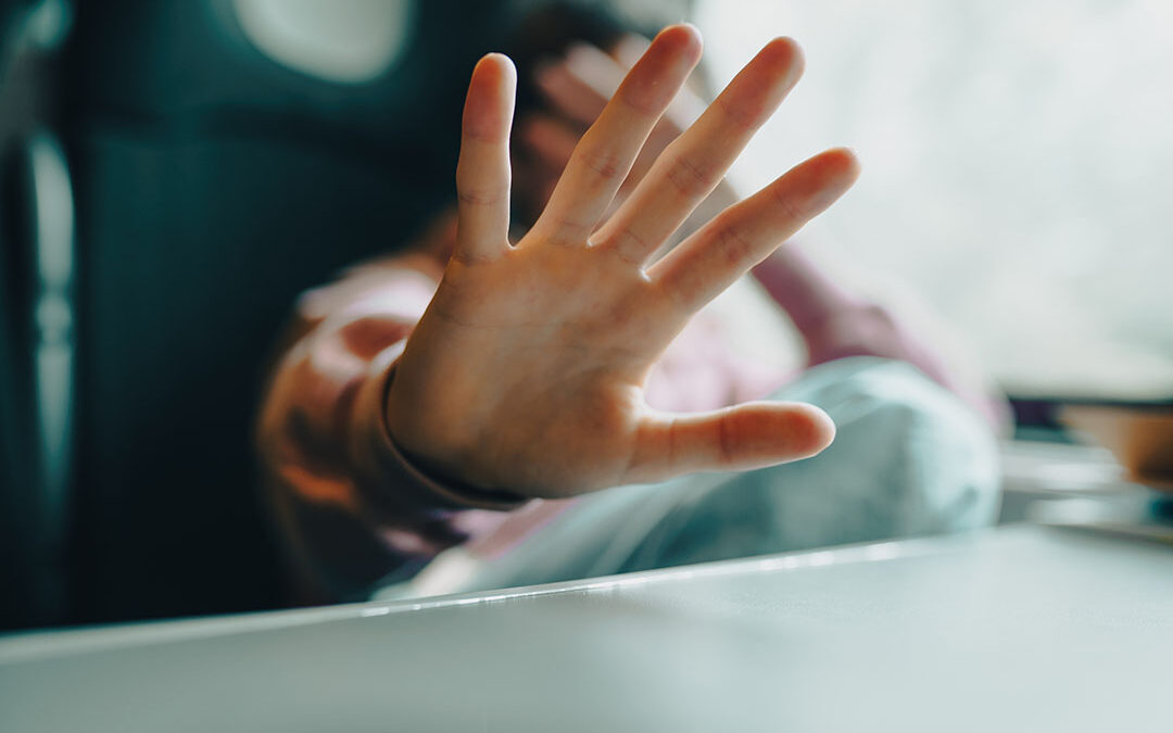 Boy holding out his hand defensively and hiding his face with the other hand