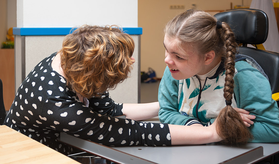 A disabled child in a wheelchair making eye contact with a special needs carer