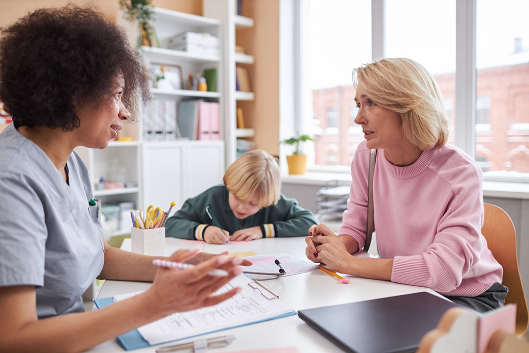 Young Mother Talking to school Therapist with Child in Background